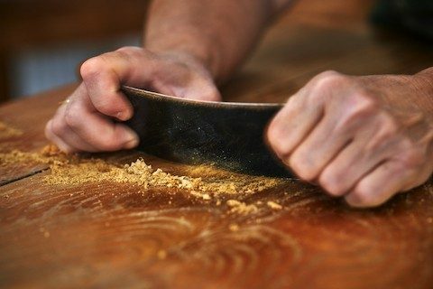 Tischlerin schabt alten Lack vom Holz